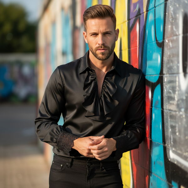 Person wearing a black ruffled-front shirt with lace cuffs beside a colorful graffiti wall
