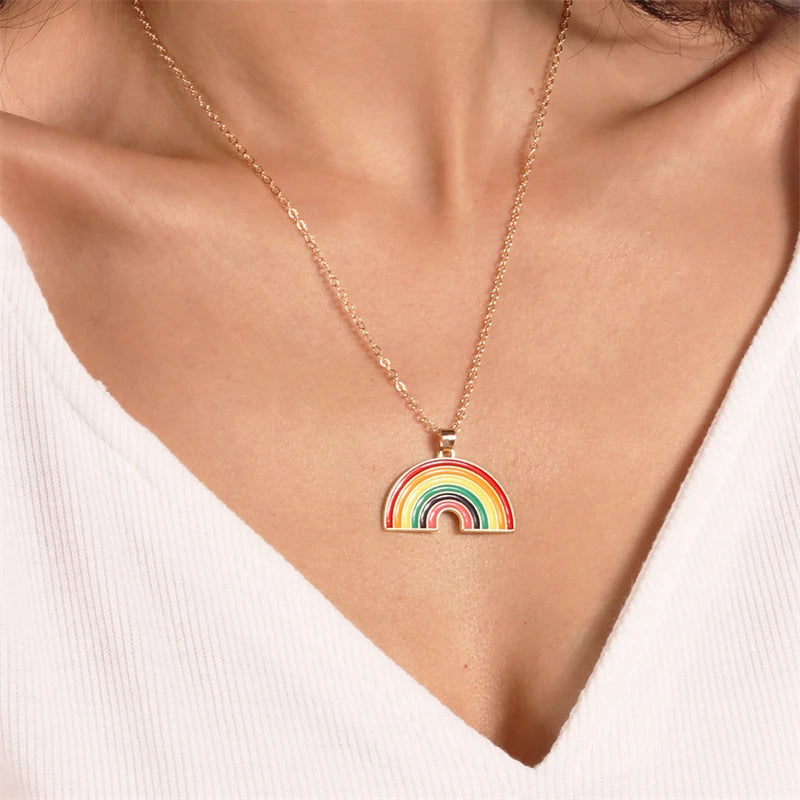 Model wearing a gold-tone rainbow pendant necklace over a white ribbed top