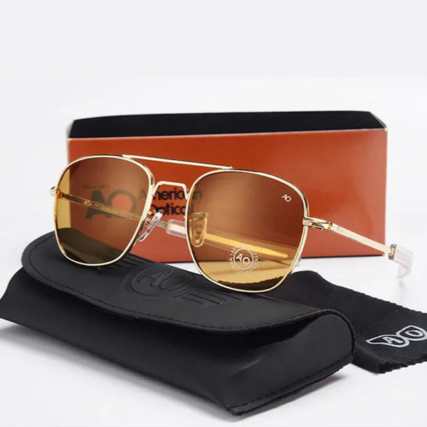 Gold aviator sunglasses with brown lenses displayed on a black case before a red box