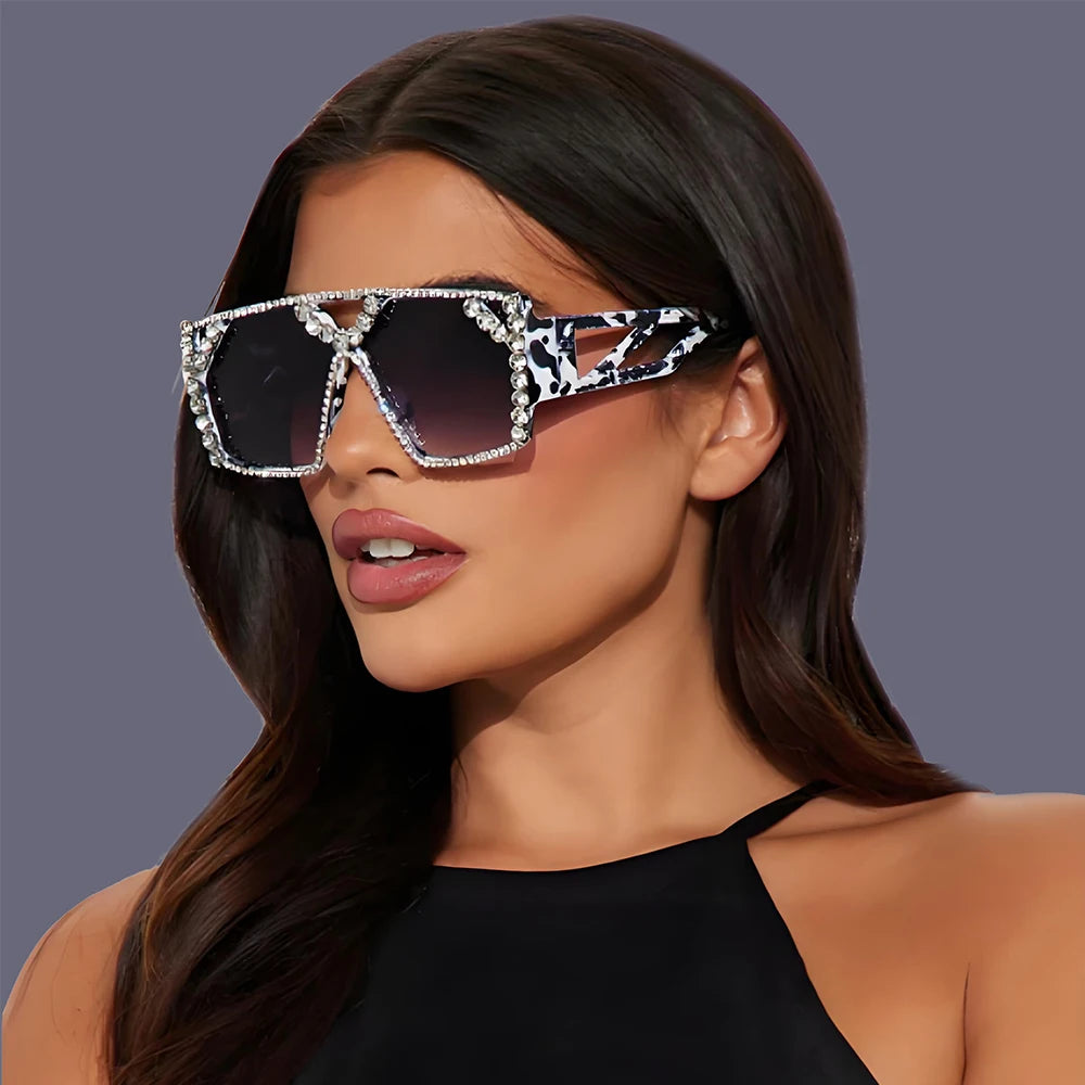 Model wearing oversized square sunglasses with rhinestone trim and patterned white-and-black arms