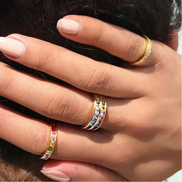 Hand wearing a rainbow-jeweled ring alongside two gold bands