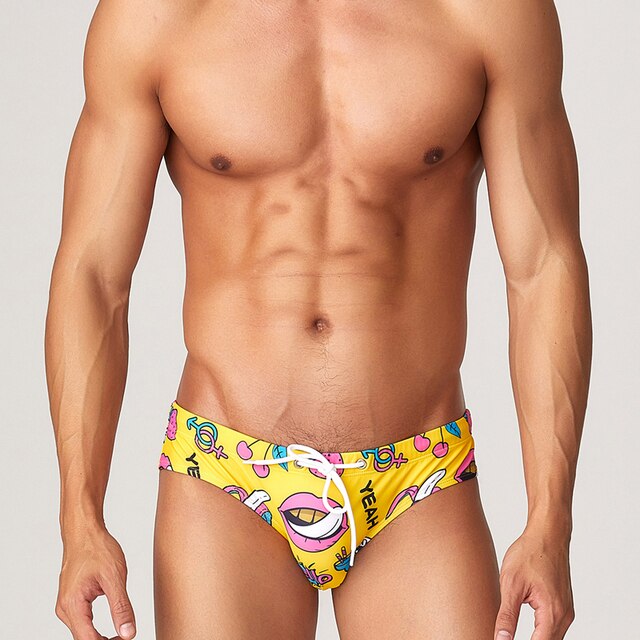 Front view of a model wearing bright yellow patterned swim briefs with a white drawstring