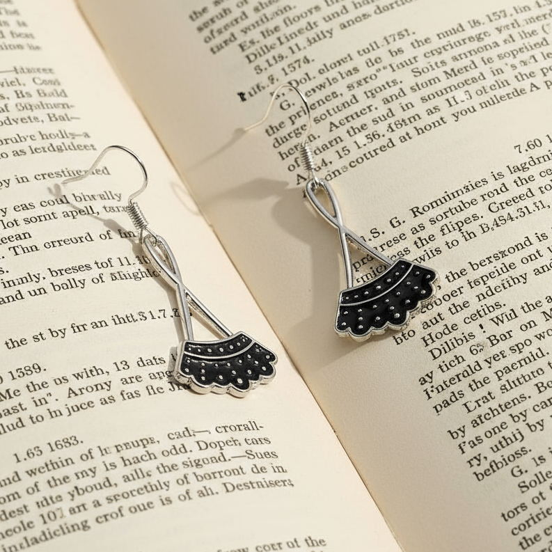 Ruth Bader Ginsburg drop earrings with black scalloped robes, displayed on an open book