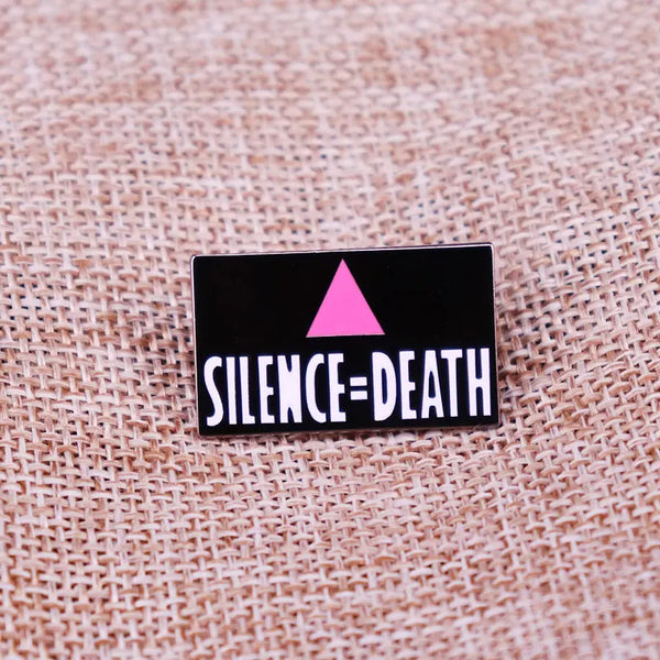 Black enamel pin reading “SILENCE=DEATH” with a pink triangle on woven fabric