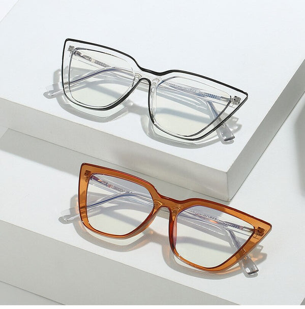 Two cat-eye glasses, one clear and one amber, displayed on white stepped blocks