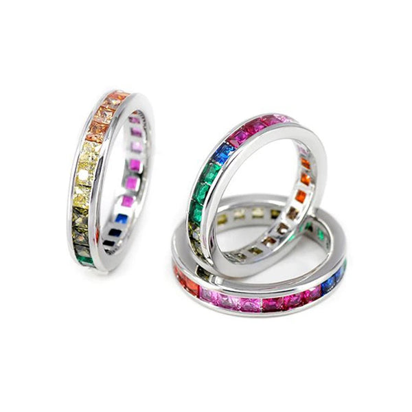 Silver-tone Pride rings with rainbow gemstone rows, stacked and arranged on a white background