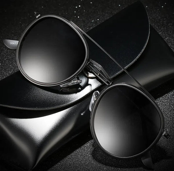 Round black sunglasses with dark lenses resting on a black case and hat