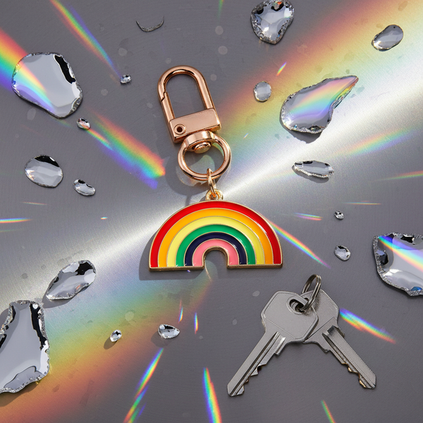 Rainbow enamel keychain with rose-gold clasp beside keys on a rainbow-reflective surface