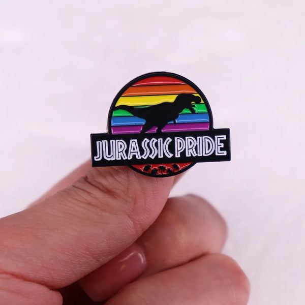 Hand holding a rainbow Jurassic Pride enamel pin with a silhouetted dinosaur