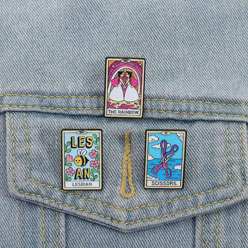 Three lesbian-themed tarot enamel pins displayed on the back pocket of light-wash denim
