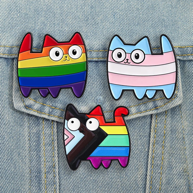 Rainbow cat enamel pins on denim, including a trans pride cat and a cat with a transgender flag detail