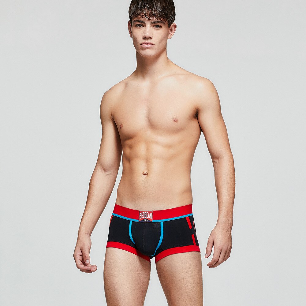Front-facing shirtless model wearing black boxer briefs with red trim and blue piping