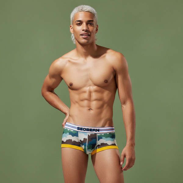 Muscular person with platinum blond hair poses in SEOBEAN Wild Comfort Mesh Camouflage Briefs, white waistband, smiling