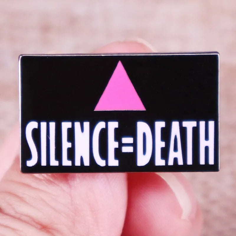 Hand holding a black Silence = Death enamel pin with a pink triangle