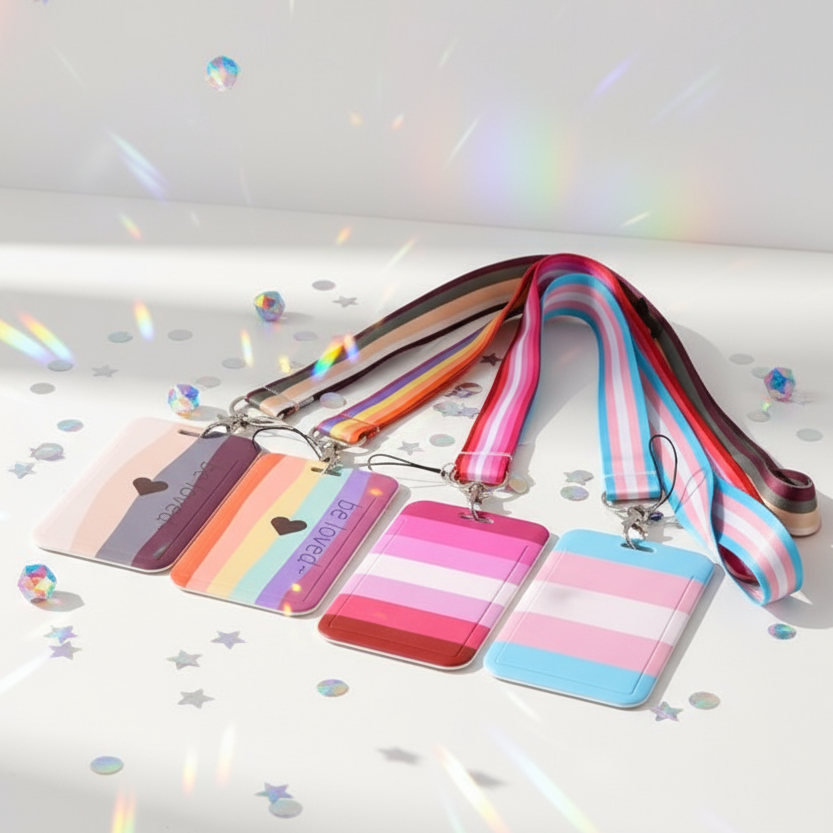 Four pastel pride-striped ID badge holders with matching lanyards, arranged on a confetti-strewn surface