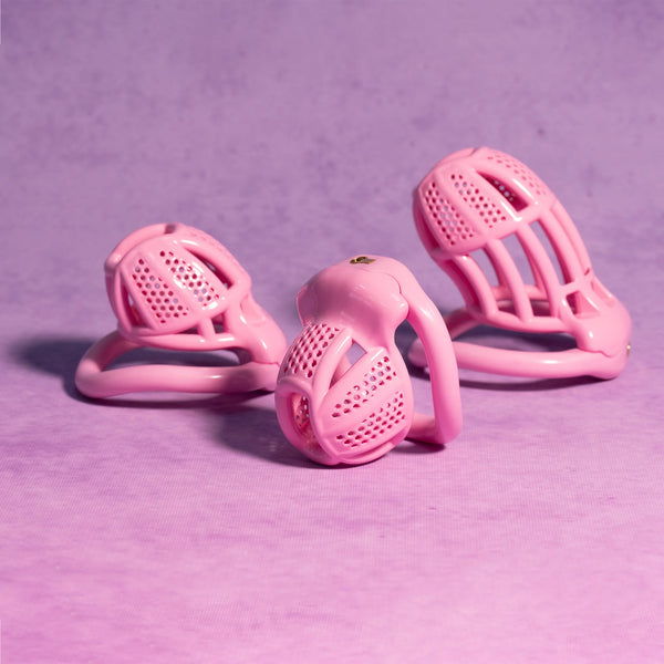 Three pink ventilated chastity cages arranged on a purple surface