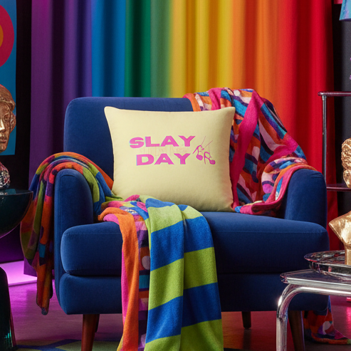 Blue armchair with "Slay The Day" pillow in bold pink text, rainbow-striped blanket, rainbow curtain