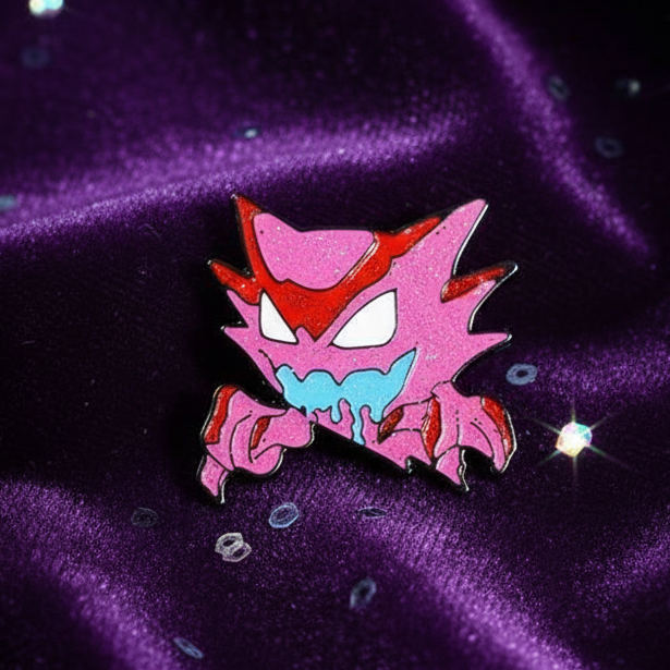 Sparkly pink Haunter enamel pin with blue mouth on purple glitter fabric