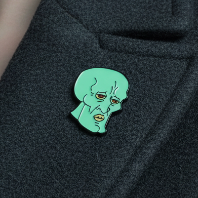 Close-up of a green Squidward enamel pin attached to black fabric