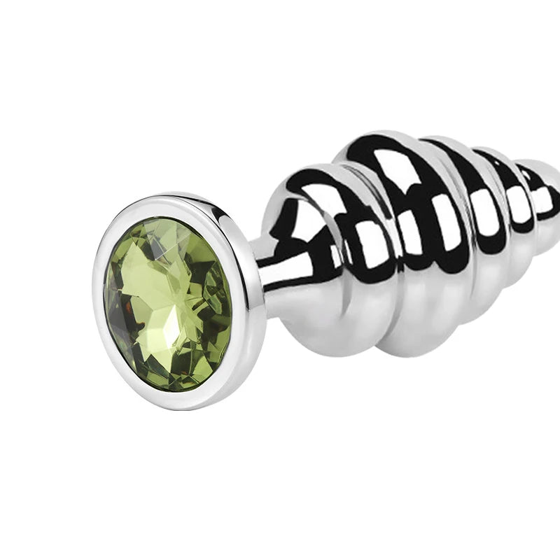 Close-up of a polished stainless steel ribbed butt plug with a large green faceted jewel