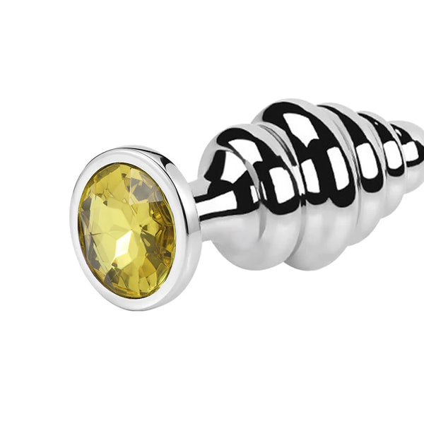 Close-up of a ribbed stainless steel butt plug with a faceted yellow jewel and flared base