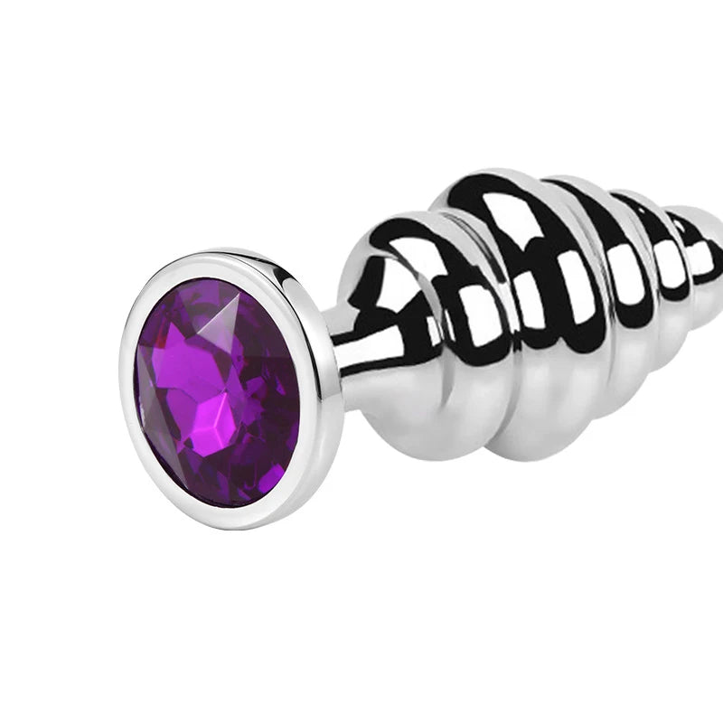 Close-up of a polished stainless steel ribbed butt plug with a large purple jewel