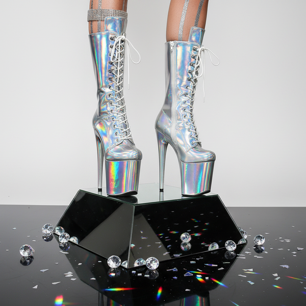 A model in holographic platform heels with rhinestone straps stands on a black mirrored pedestal