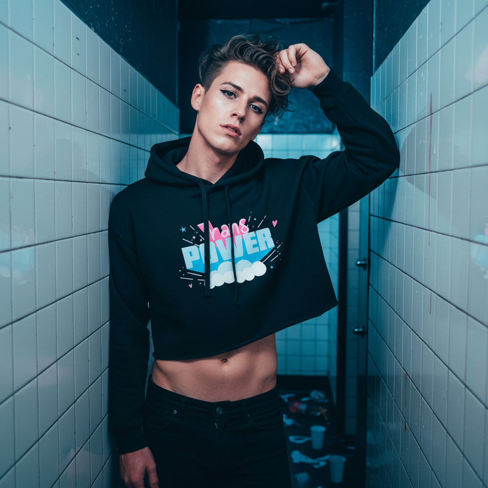 Black "Stand Proud Trans Power" crop hoodie in colorful lettering, worn by a short-haired person beaming with queer pride