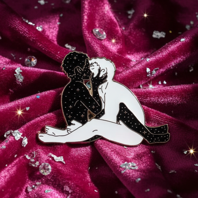 Enamel pin showing two star-speckled men kissing on a glittering magenta fabric background