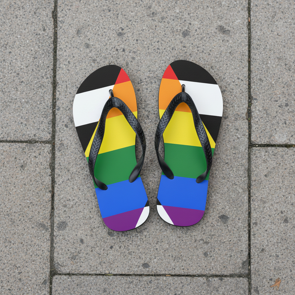 Straight Ally flip-flops with bold black-and-white stripes and a rainbow chevron, side by side on light gray stone pavement.