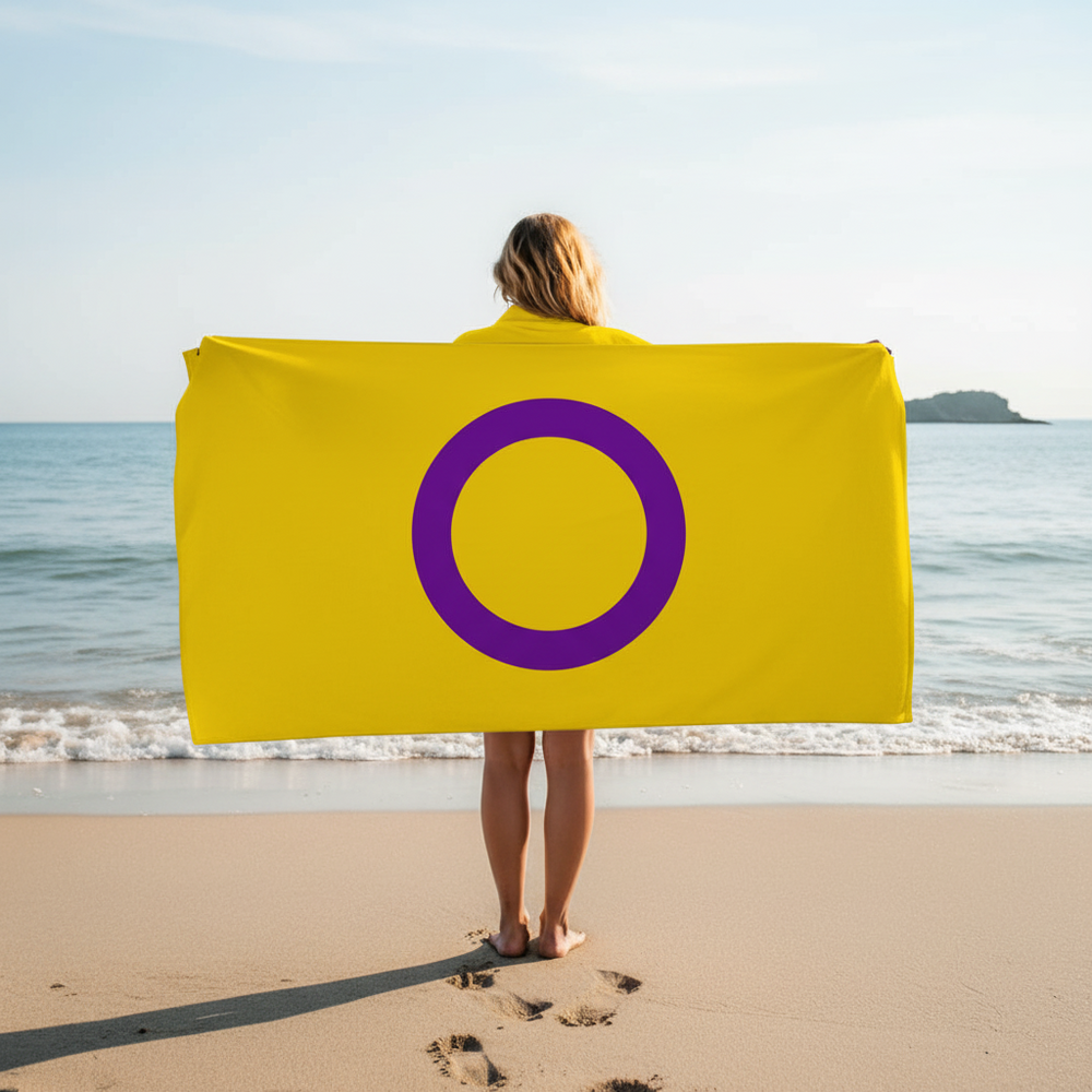 Intersex Pride Flag Towel—bold yellow cotton with a purple circle—held by a barefoot person on sand, queer joy by the sea.