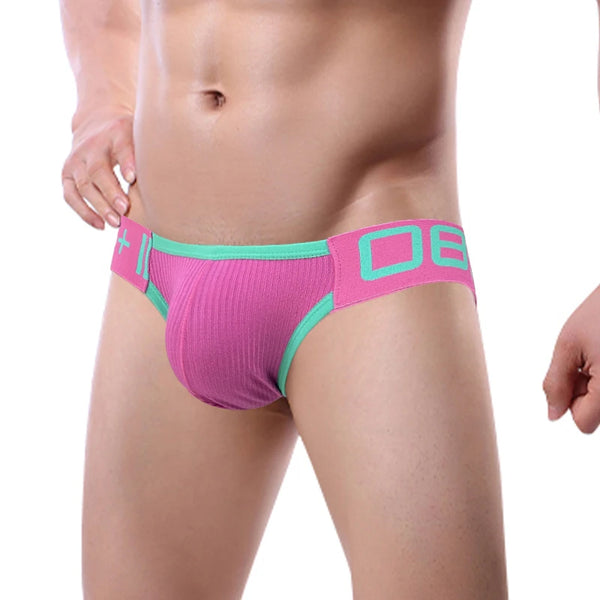 Front three-quarter view of a model wearing a pink mesh jockstrap with turquoise trim and waistband lettering