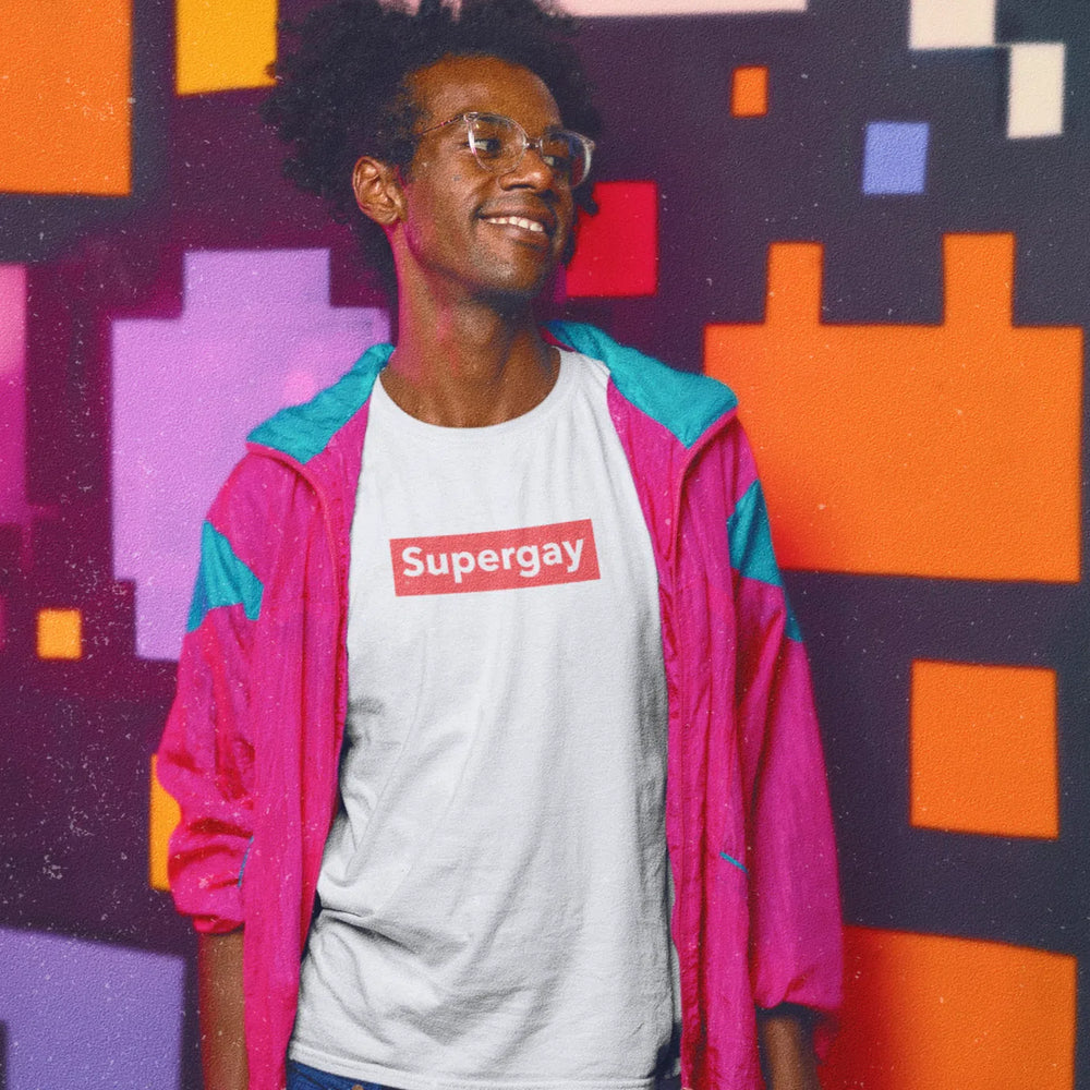 Model wearing a white Supergay T-shirt with a red chest logo, against a colorful geometric wall