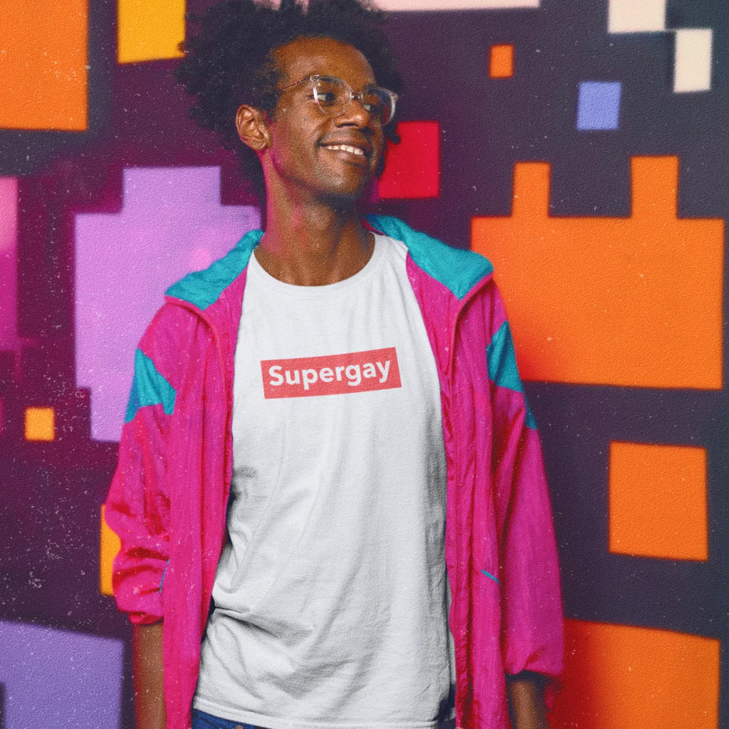 Model wearing a white Supergay T-shirt with a red chest logo, against a colorful geometric wall