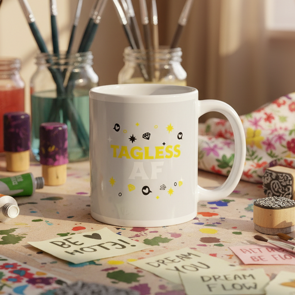 White mug reading “TAGLESS AF” on a paint-splattered craft table
