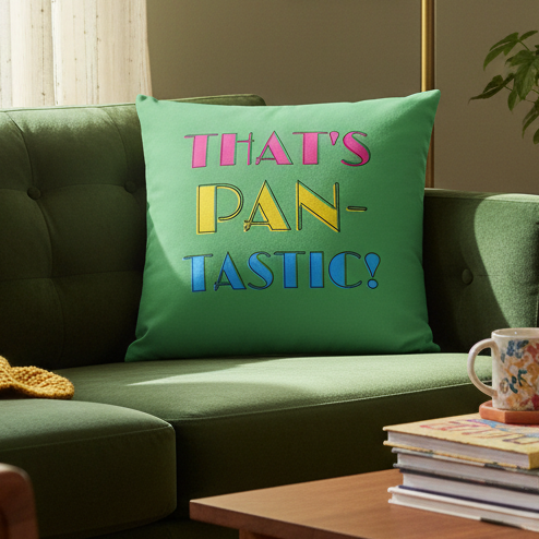 A green couch with a "That's Pan-tastic!" pillow in playful text. Coffee table holds yellow knit, mug, books