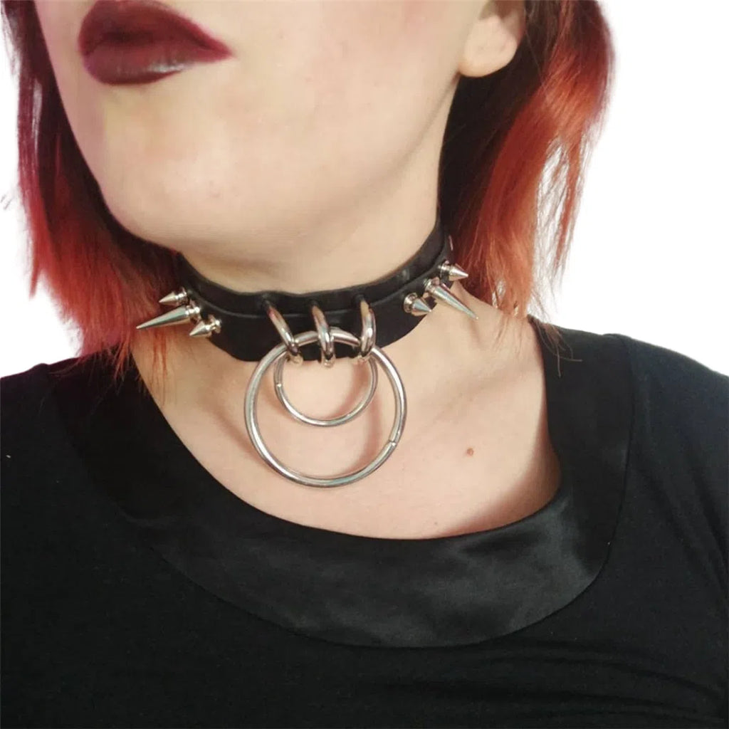 Close-up of a person wearing a black spiked collar with two large silver rings