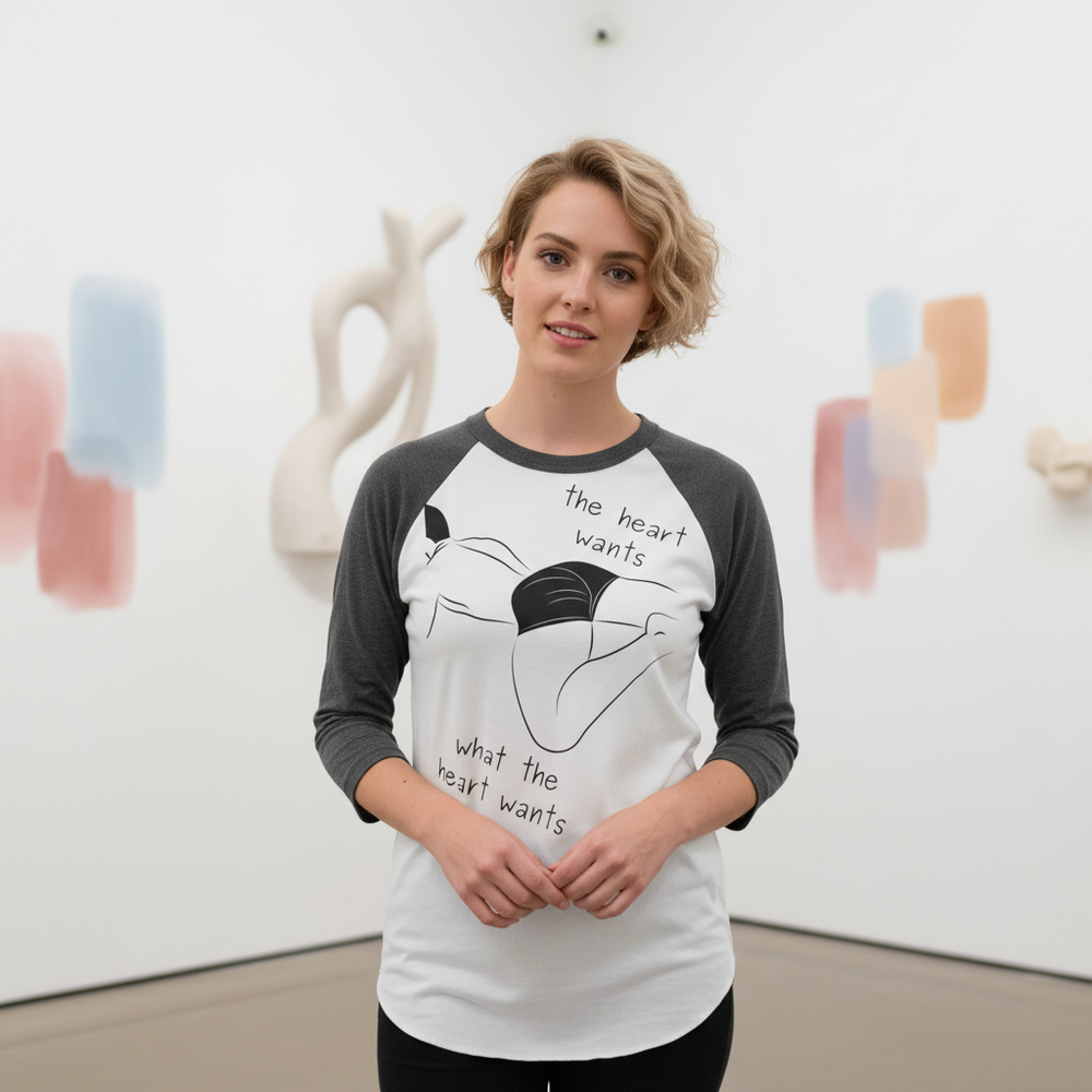 Model wearing a white and charcoal raglan shirt reading “the heart wants what the heart wants”