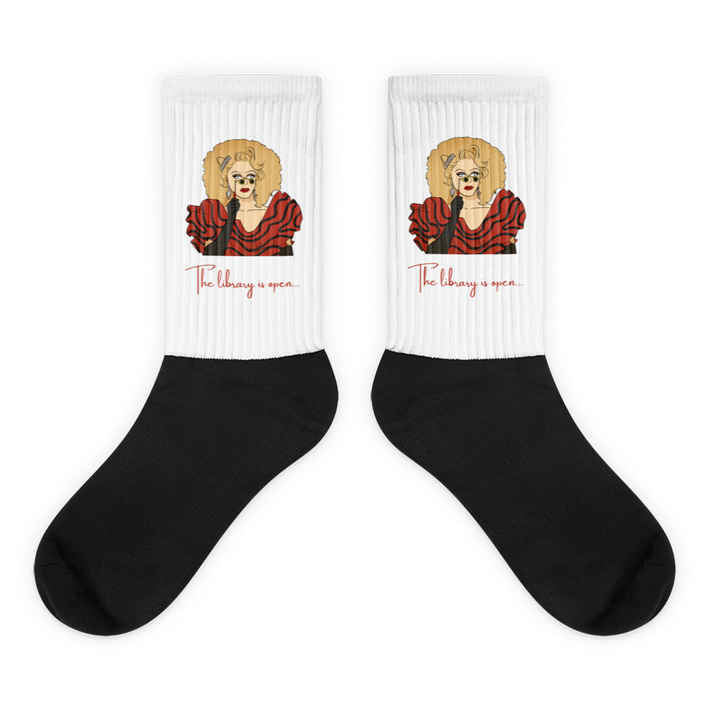 Pair of black-and-white crew socks with a red-dressed illustrated figure and “The library is open...”