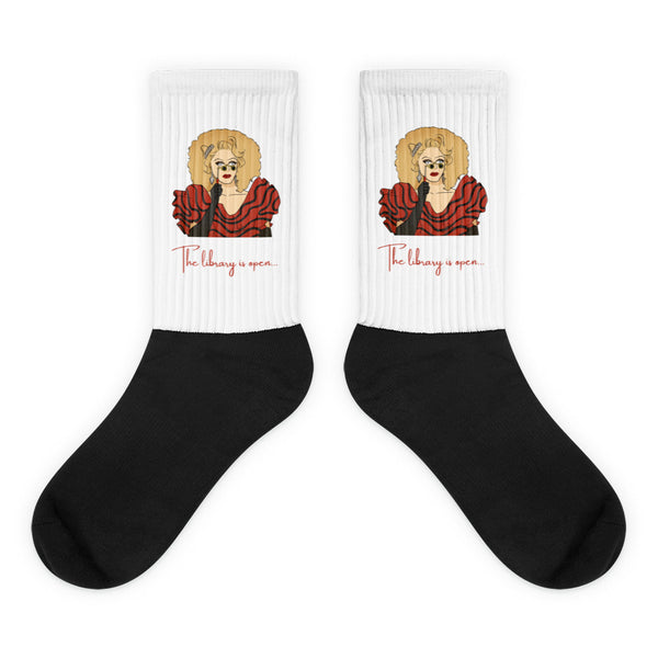 Pair of black-and-white crew socks with a red-dressed illustrated figure and “The library is open...”