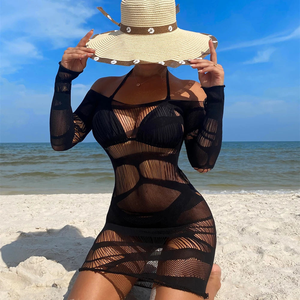 Front view of a model in a sheer black mesh dress and sun hat on a beach