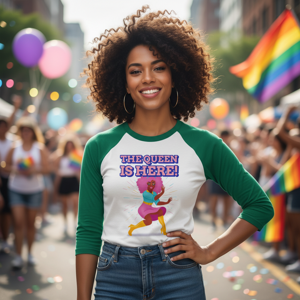 Smiling person at a Pride parade wearing a green-sleeved shirt reading “THE QUEEN IS HERE!”