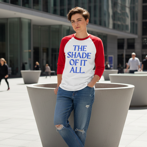 Person wearing a white-and-red raglan shirt reading “THE SHADE OF IT ALL.”