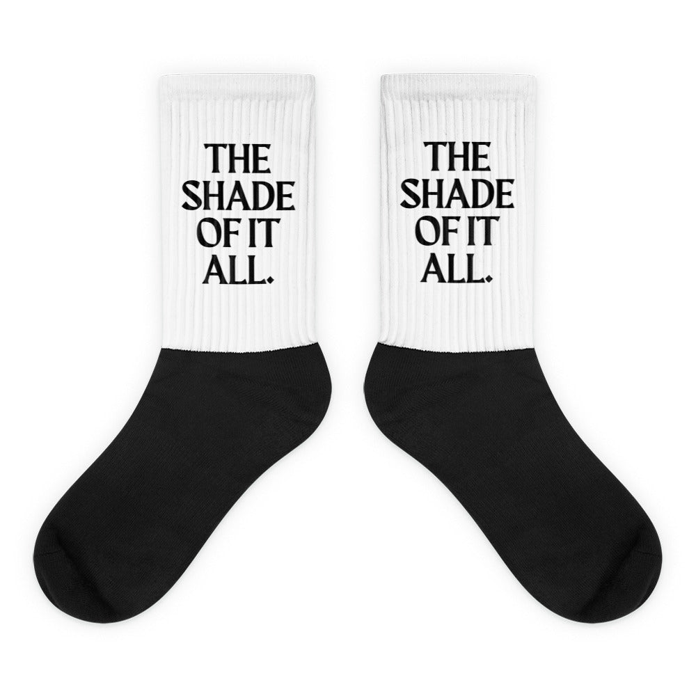 Pair of black-and-white socks with ribbed cuffs reading “THE SHADE OF IT ALL.”