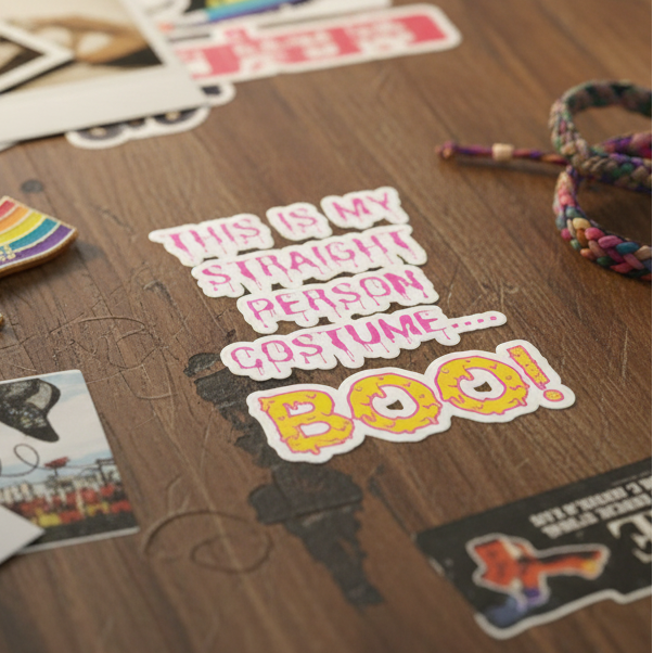 Close-up of a pink-and-yellow sticker reading “THIS IS MY STRAIGHT PERSON…BOO!” on a wooden table