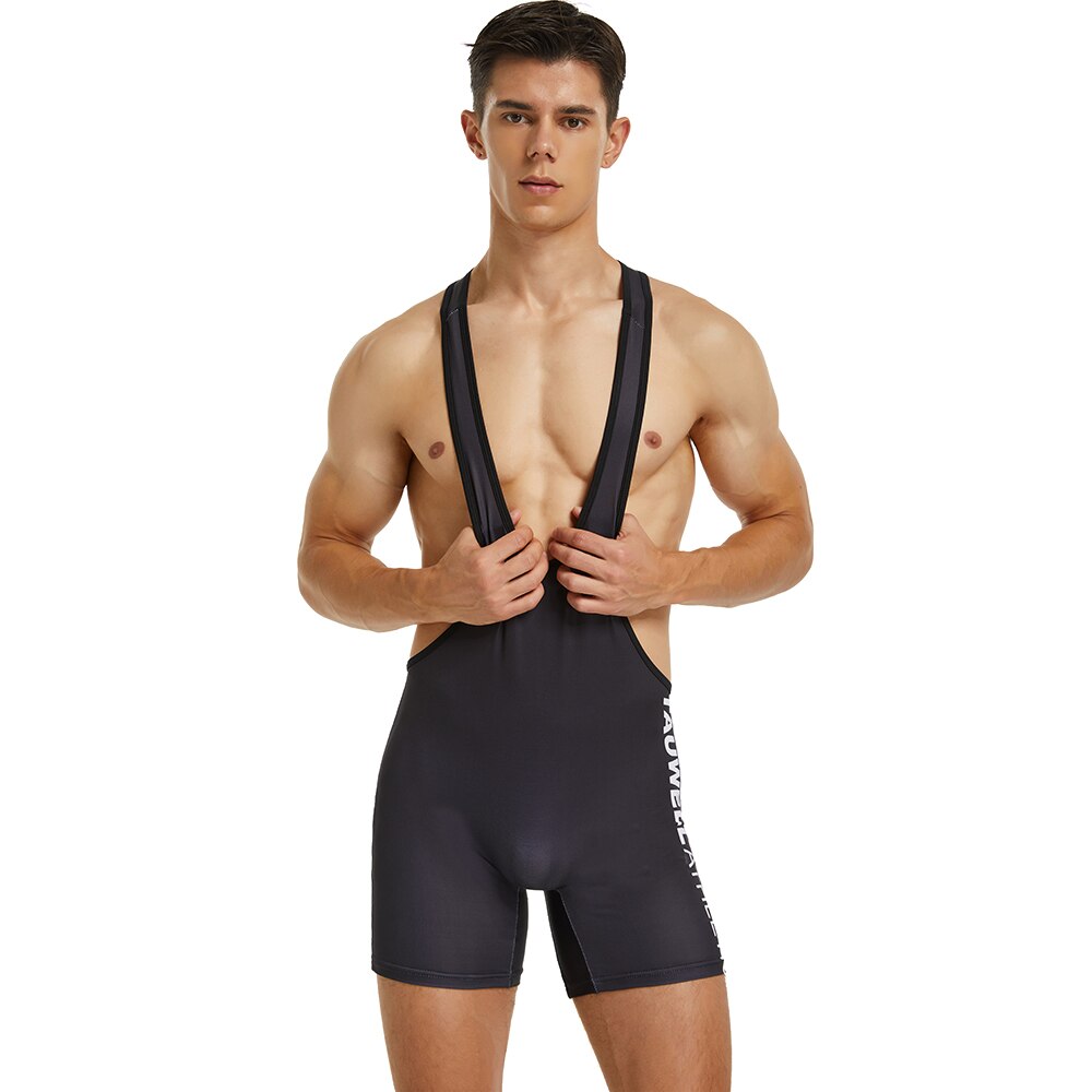 Front-facing model wearing a black wrestling-style bodysuit with wide shoulder straps