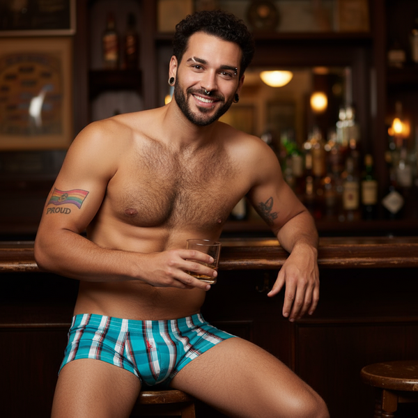 At a bar, a smiling model wears turquoise, white, and red plaid boxer briefs