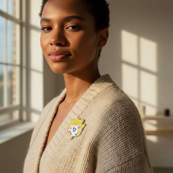 Togepi enamel pin with yellow and white character design on a beige cardigan