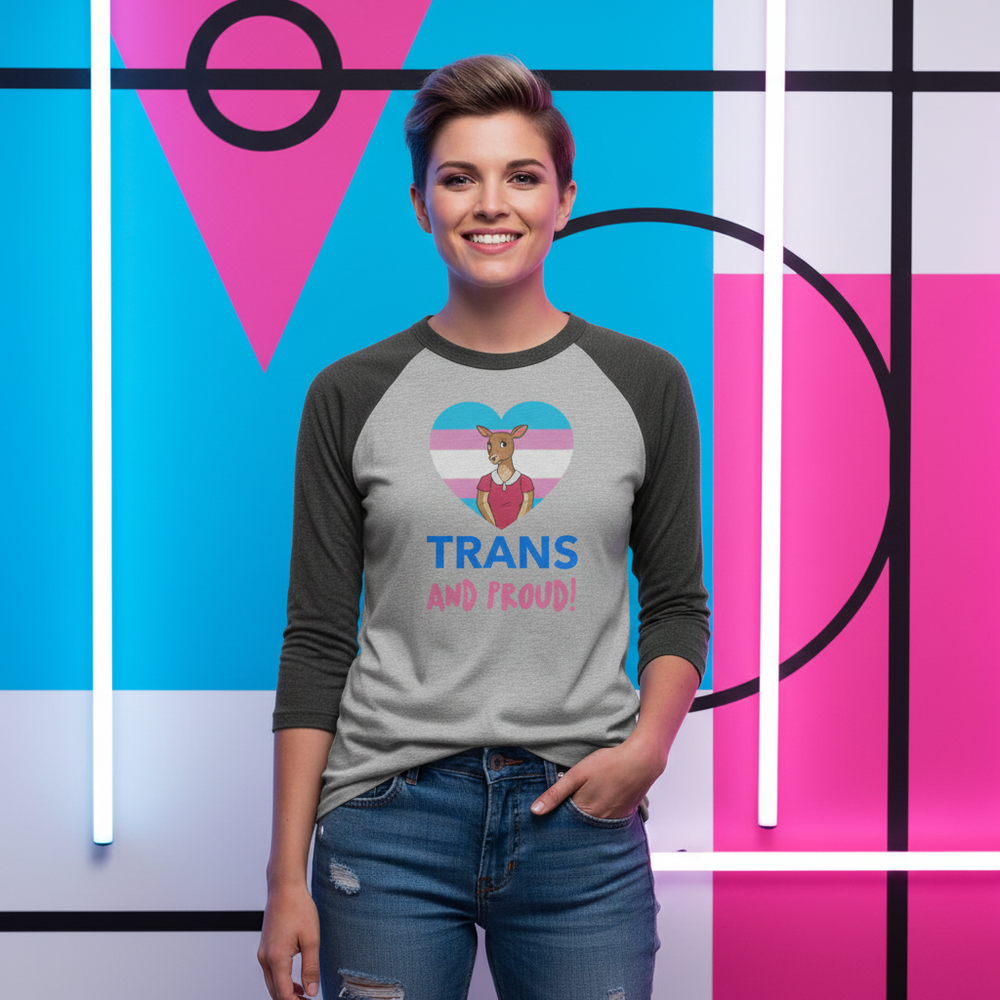 Smiling model wearing a gray raglan shirt with a heart, deer, and “TRANS AND PROUD!”