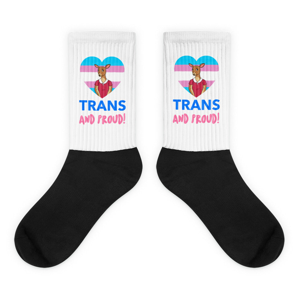 Pair of black-and-white crew socks with trans pride hearts, deer, and “TRANS AND PROUD!” text